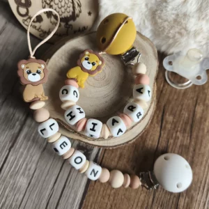 Deux attaches tétines personnalisées lion en silicone : un modèle dans des tons beige et marron, l'autre dans des tons pêche et moutarde, personnalisables avec le prénom de bébé – Babybou-Créa