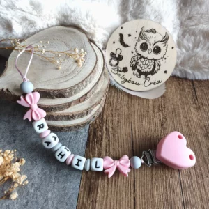 Attache tétine personnalisée en silicone avec doubles nœuds roses, perles roses, grises et blanches et clip cœur rose. Création réalisée avec soin par Babybou-Créa.