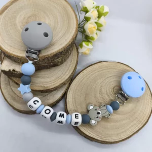 Attache doudou personnalisée en silicone avec deux clips en silicone, motif koala, perles dans les tons gris et bleu et prénom Come. Création réalisée avec soin pour bébé.