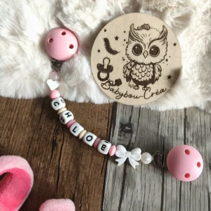 Attache doudou personnalisée en silicone avec deux clips roses, nœud blanc, perles roses et beiges, personnalisée avec le prénom Chloé. Babybou-Créa