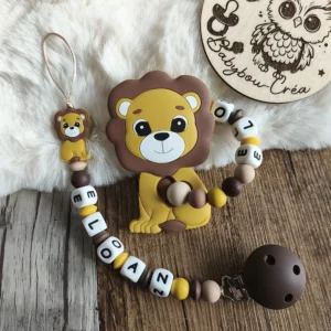 Attache tétine personnalisée et anneau de dentition en silicone sur le thème lion, assortis avec des perles marron, beige et jaune. Les deux créations sont personnalisées avec le prénom « LOAN » et présentées sur un fond en bois dans une ambiance douce et naturelle. Babybou-Créa