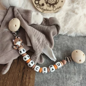 Attache doudou personnalisée Renard en bois et silicone avec deux clips en bois, motif renard et prénom personnalisé, présentée avec un doudou. Babybou-Créa